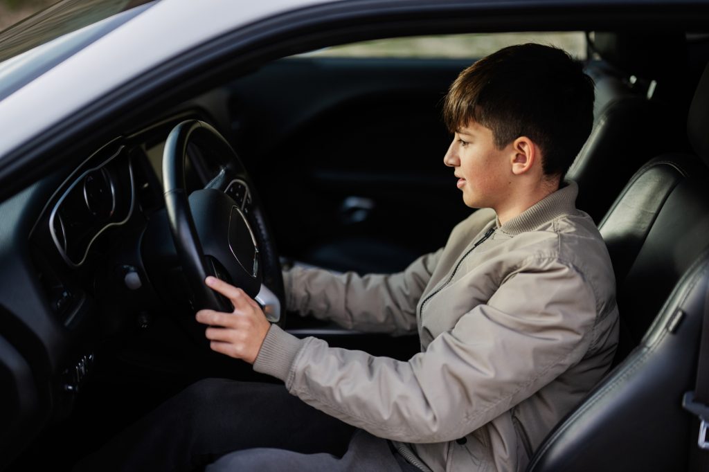 Teenager boy sit in muscle car. Young teen driver.