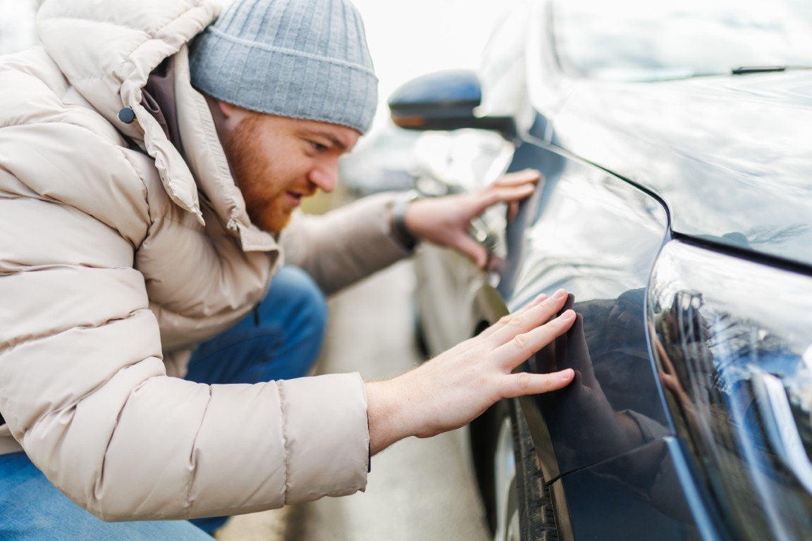 Contemplation and despair a young adult man stands beside a broken scratches car, clearly frustrated and displeased